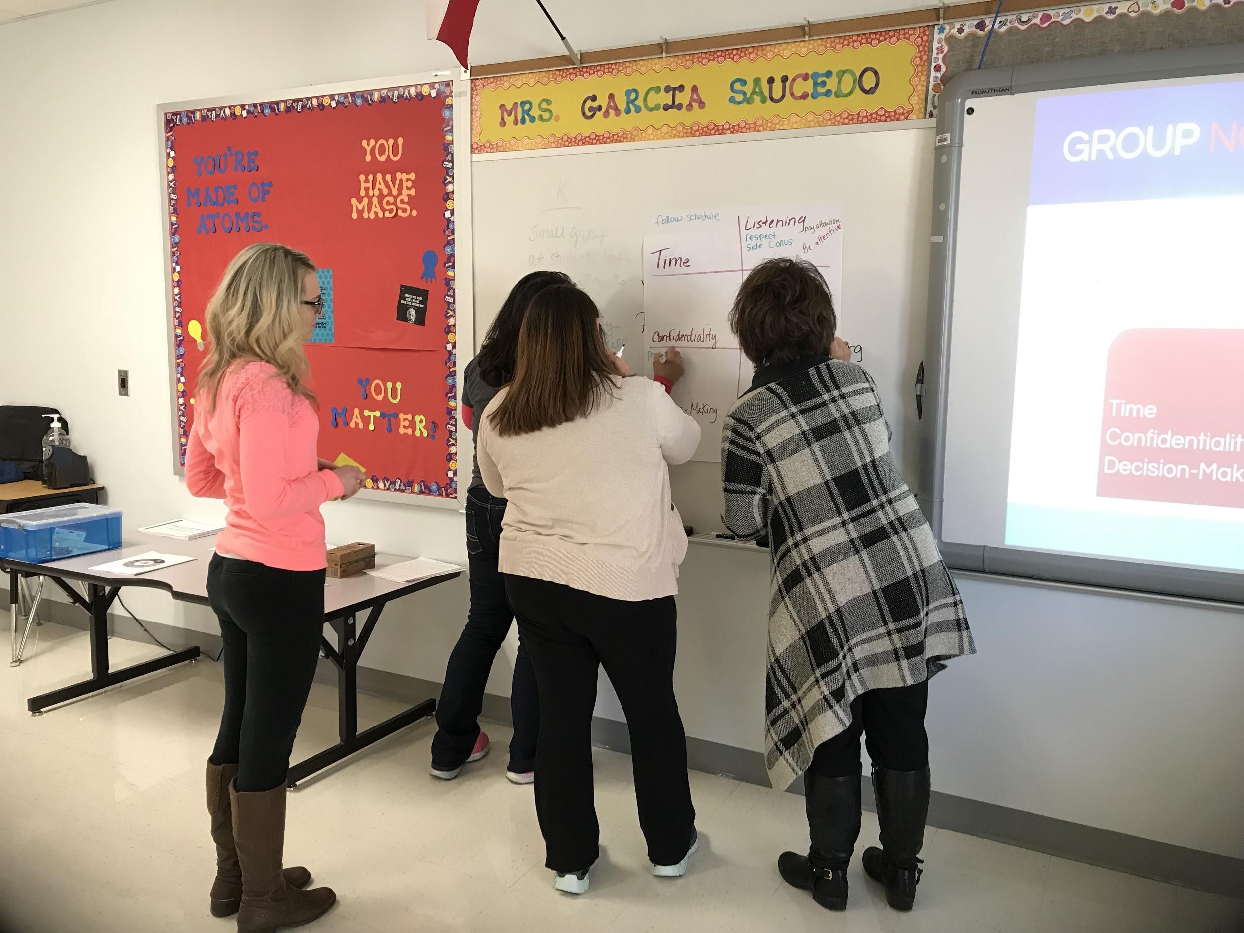 Teachers writing assignment info on a whiteboard